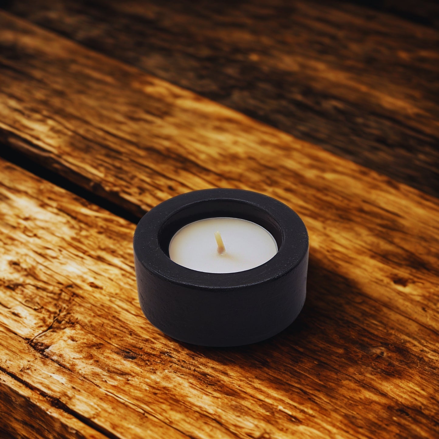 Black candle holder with a white candle on a wooden surface