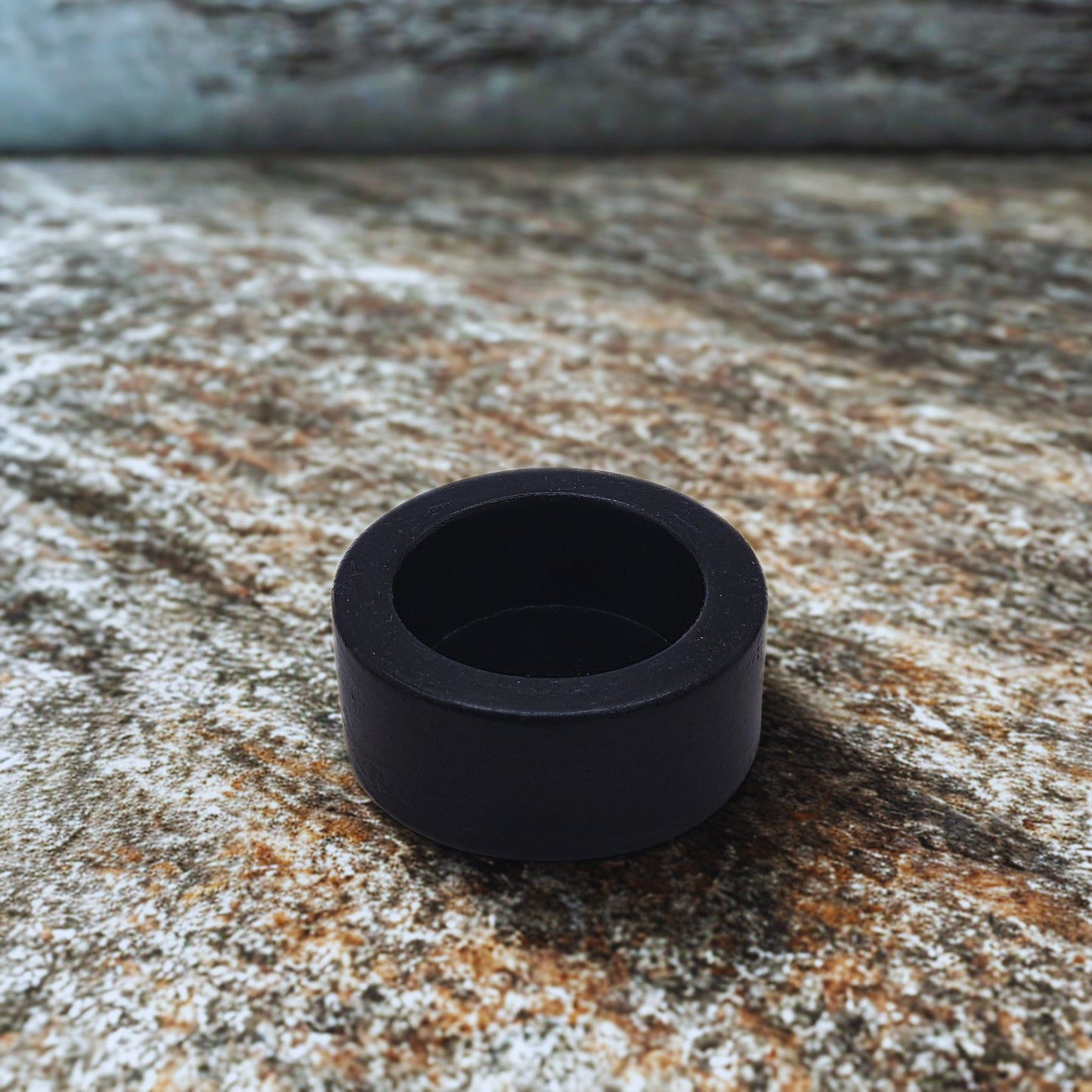 Black round tealight holder on a textured stone surface
