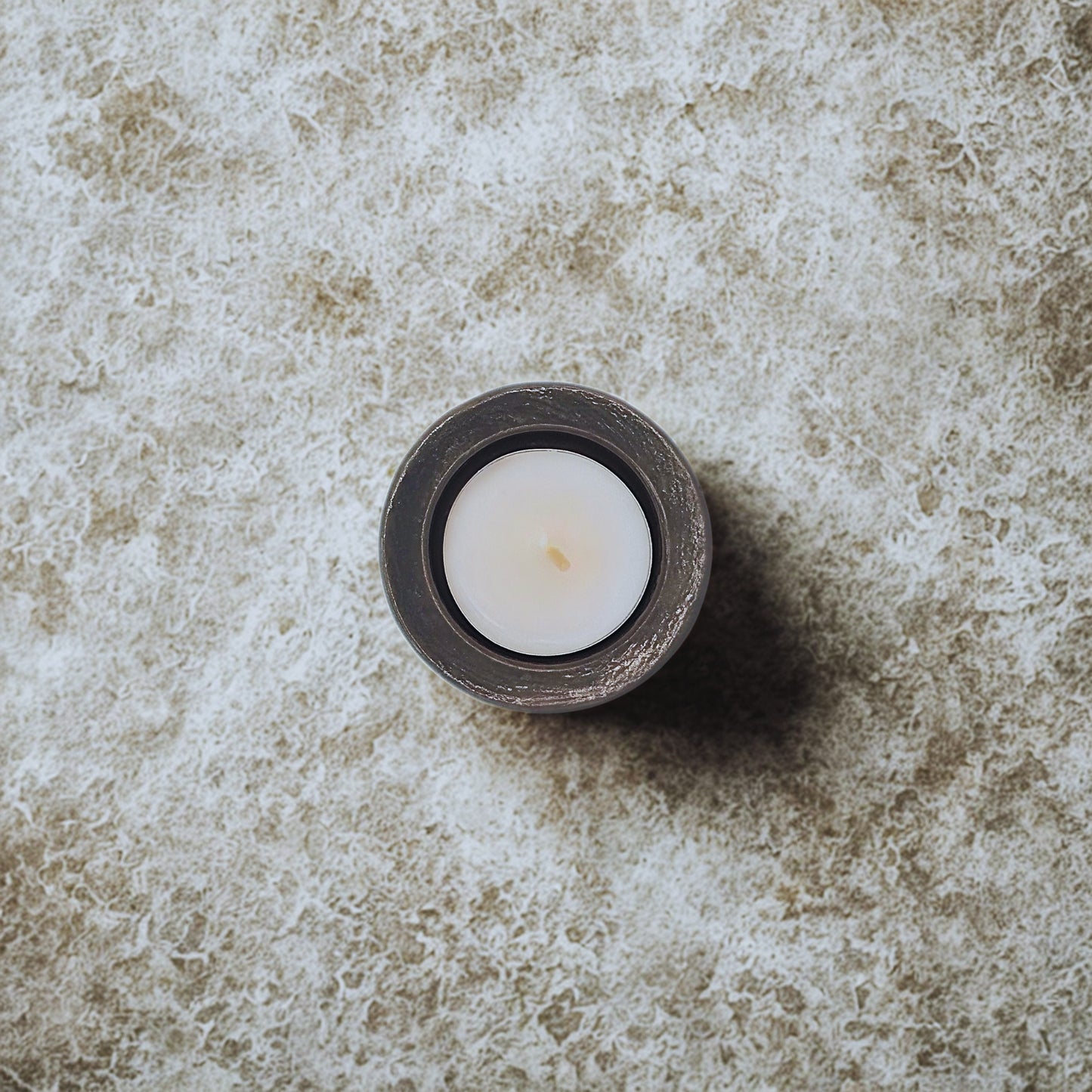 White candle in a dark holder on a textured stone surface