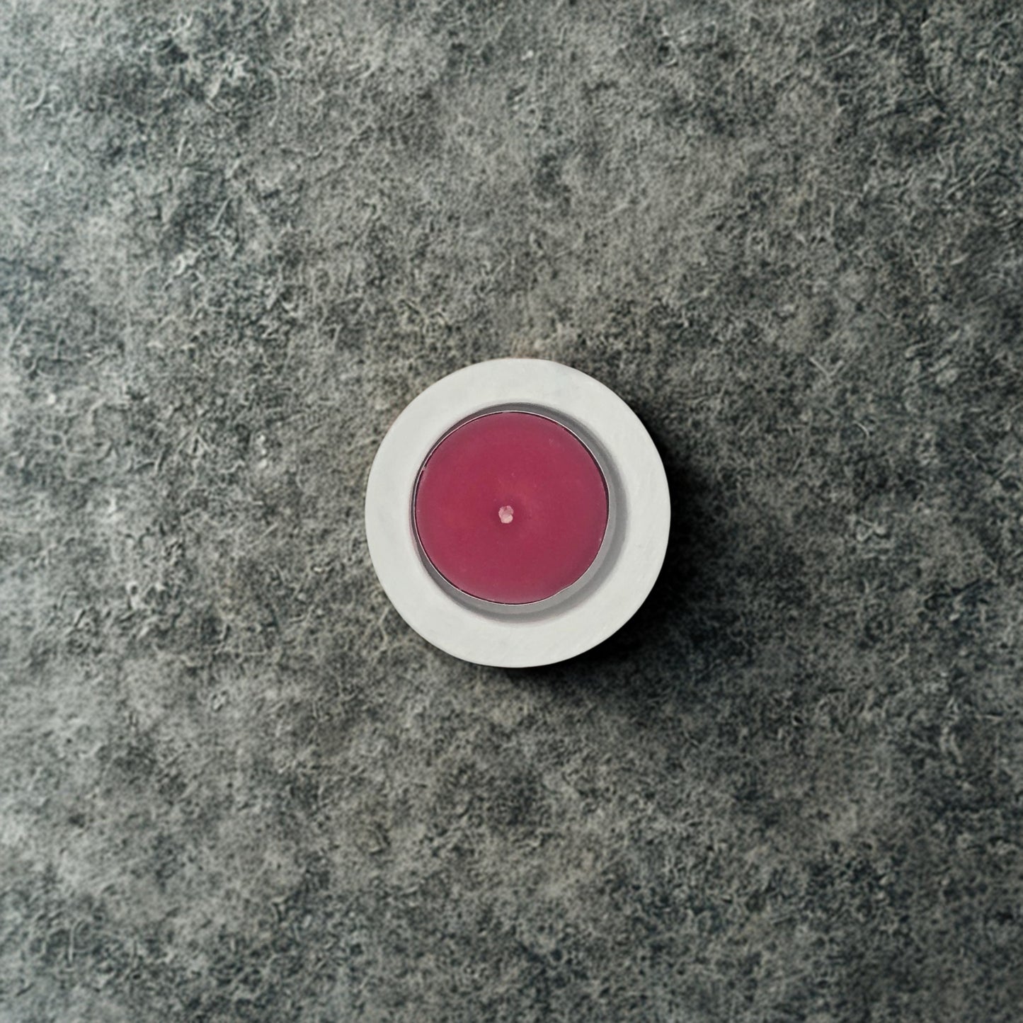 Pink candle in a white holder on a gray stone surface