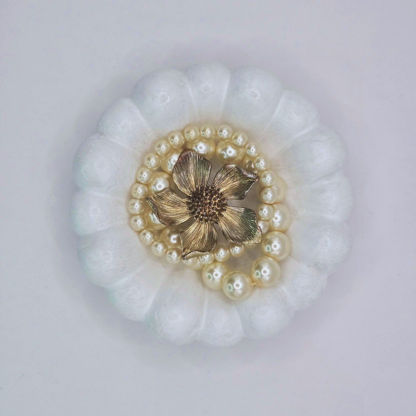 Decorative brooch with gold center and pearl accents on a white background