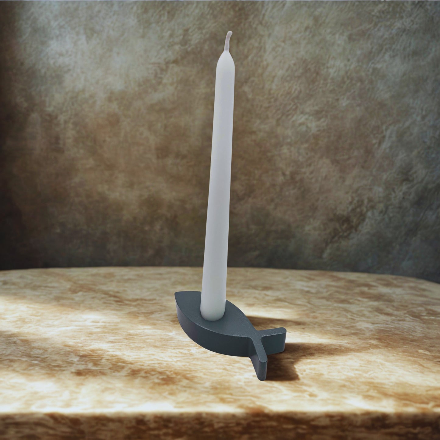 Gray candle holder with a white candle on a wooden surface
