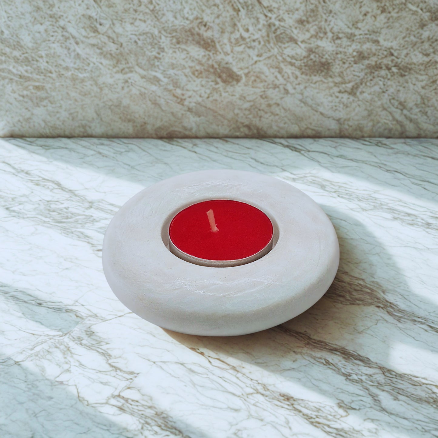 Red candle in a white Flat round tealight holder on a marble surface