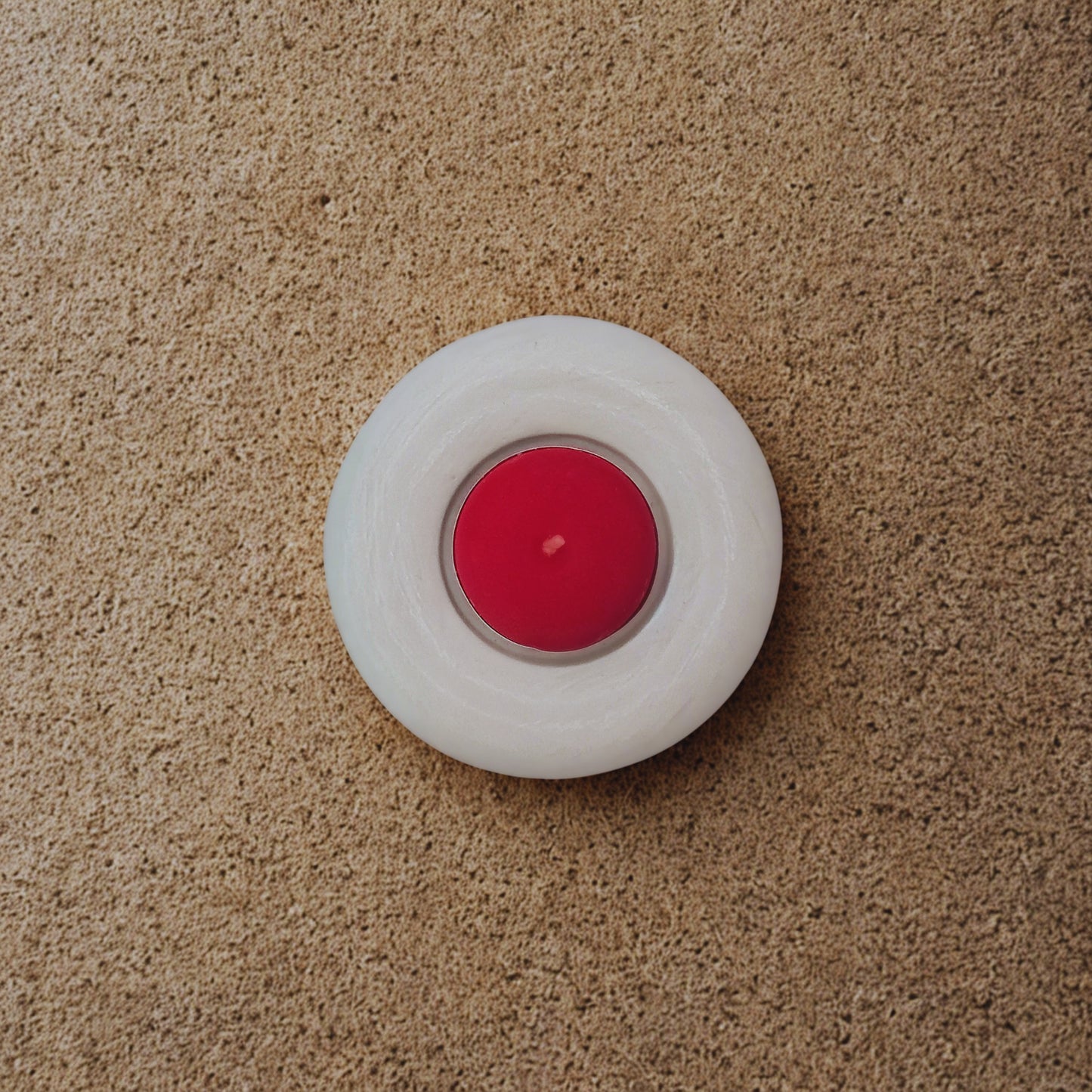 Red candle in a white holder on a beige carpet