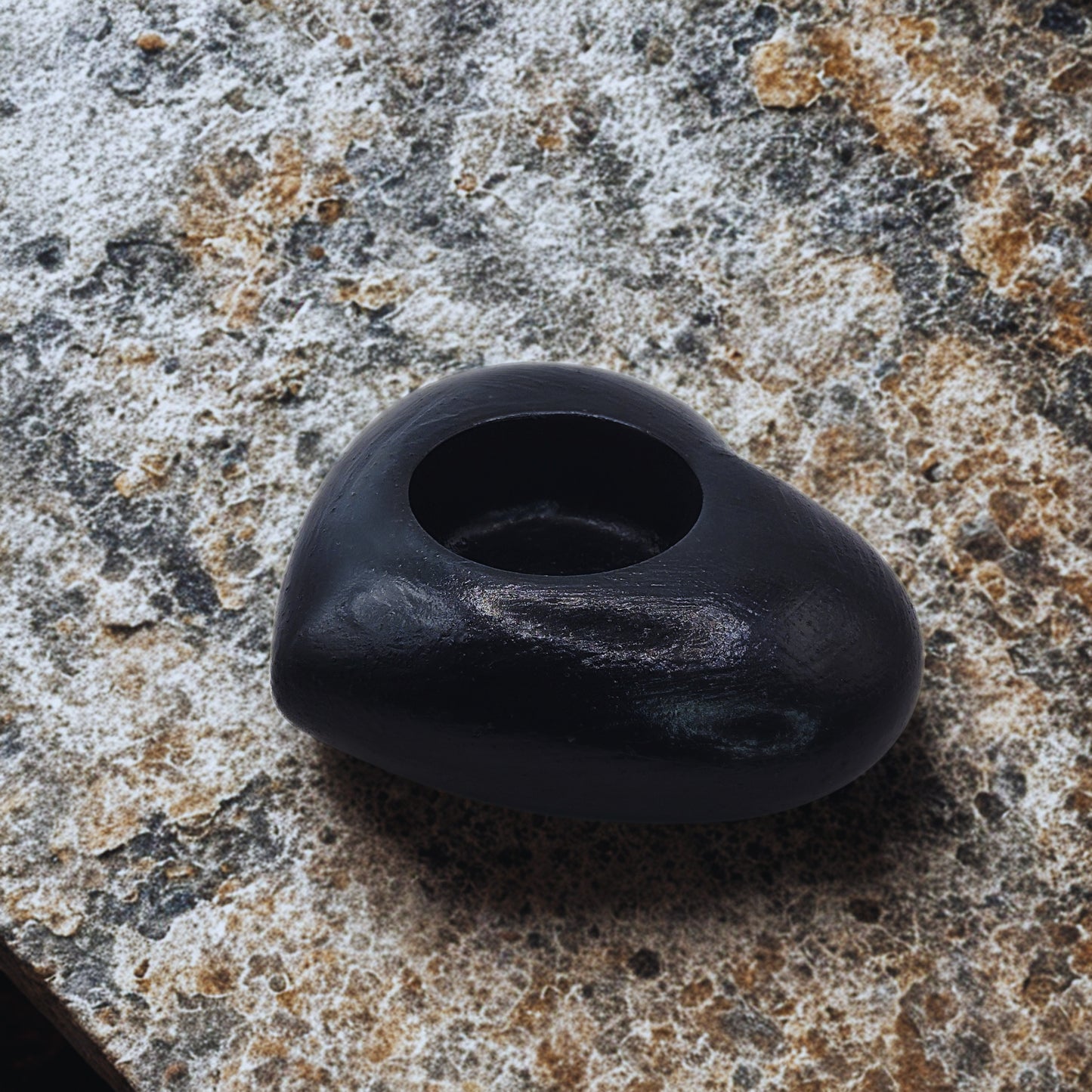 Black Heart tealight holder with a hole on a textured surface