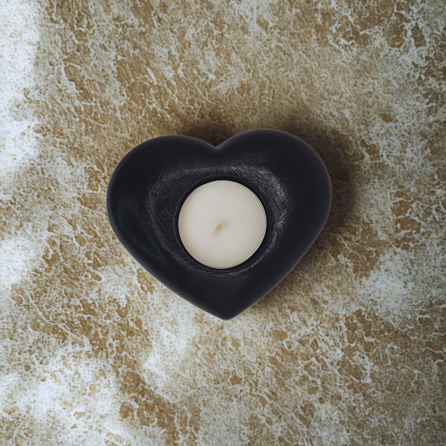 Heart tealight holder with a white candle on a textured beige surface