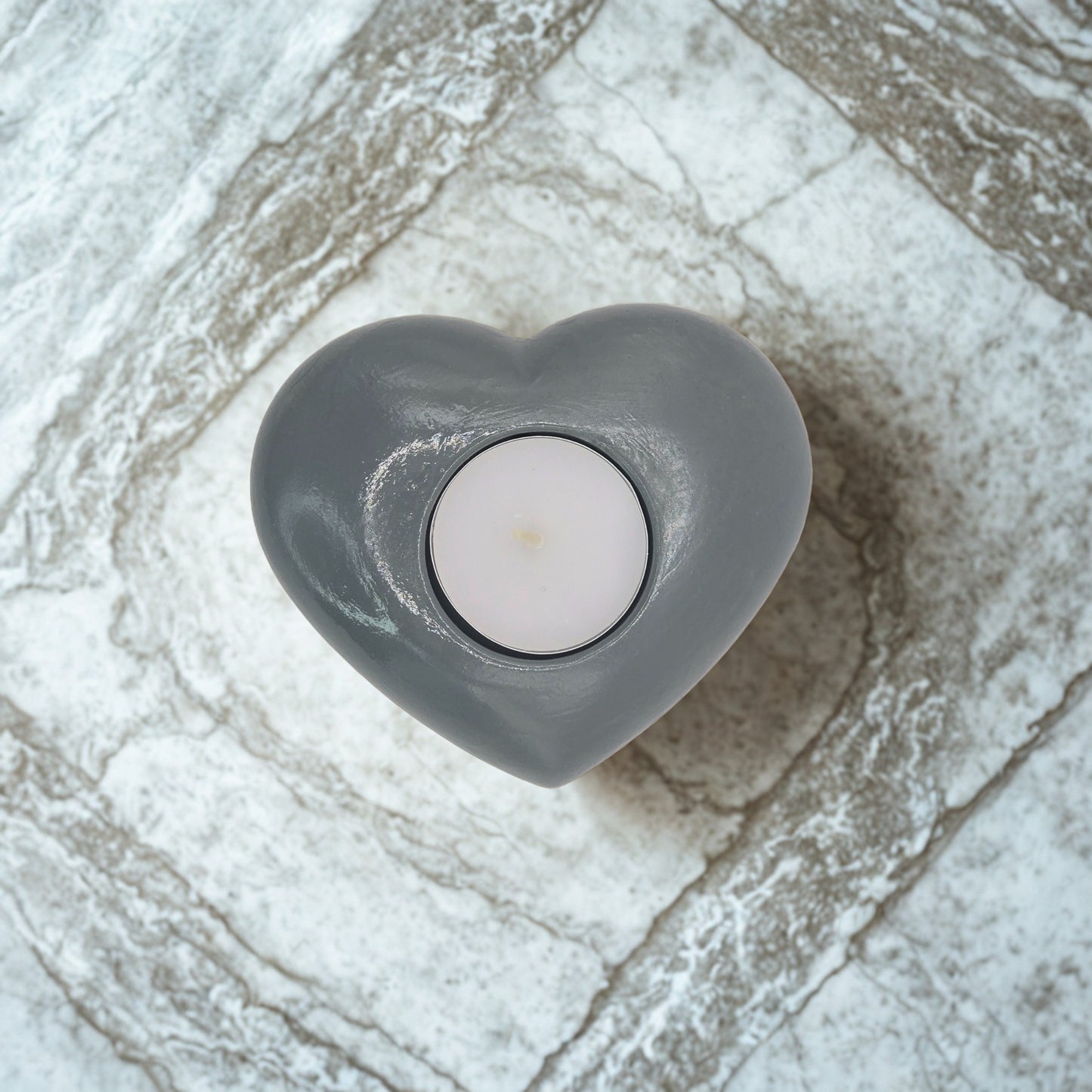 Heart-shaped gray candle holder with a white candle on a stone surface