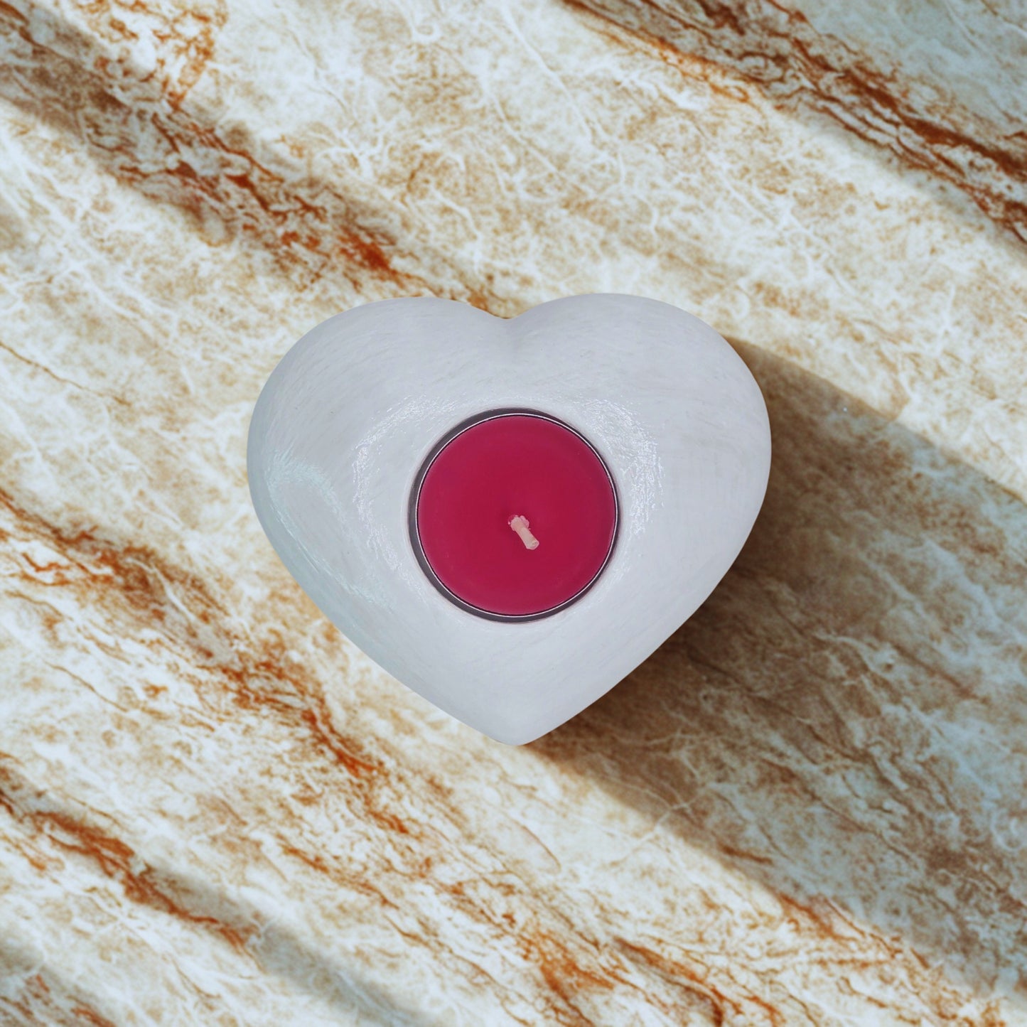 Heart tealight holder with a pink wick on a marble surface