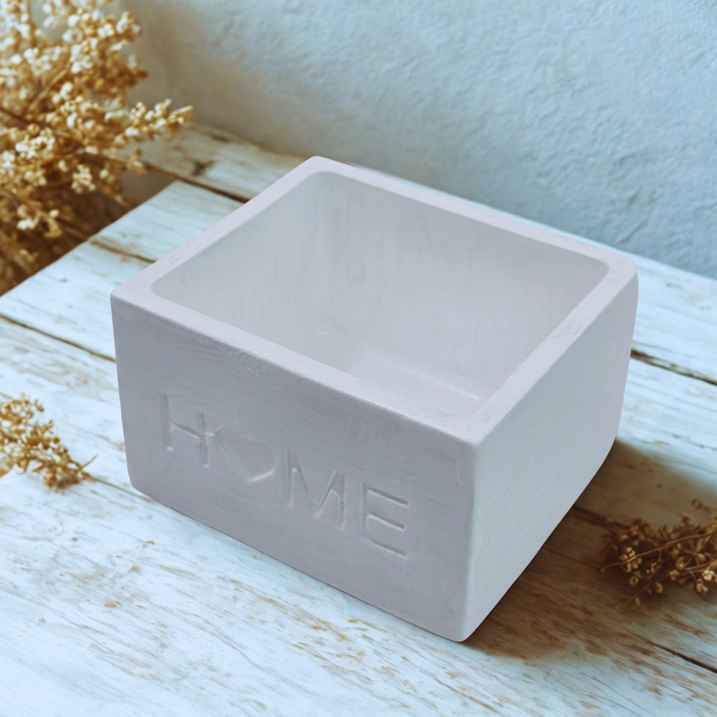 Home planter on a wooden surface with dried flowers.