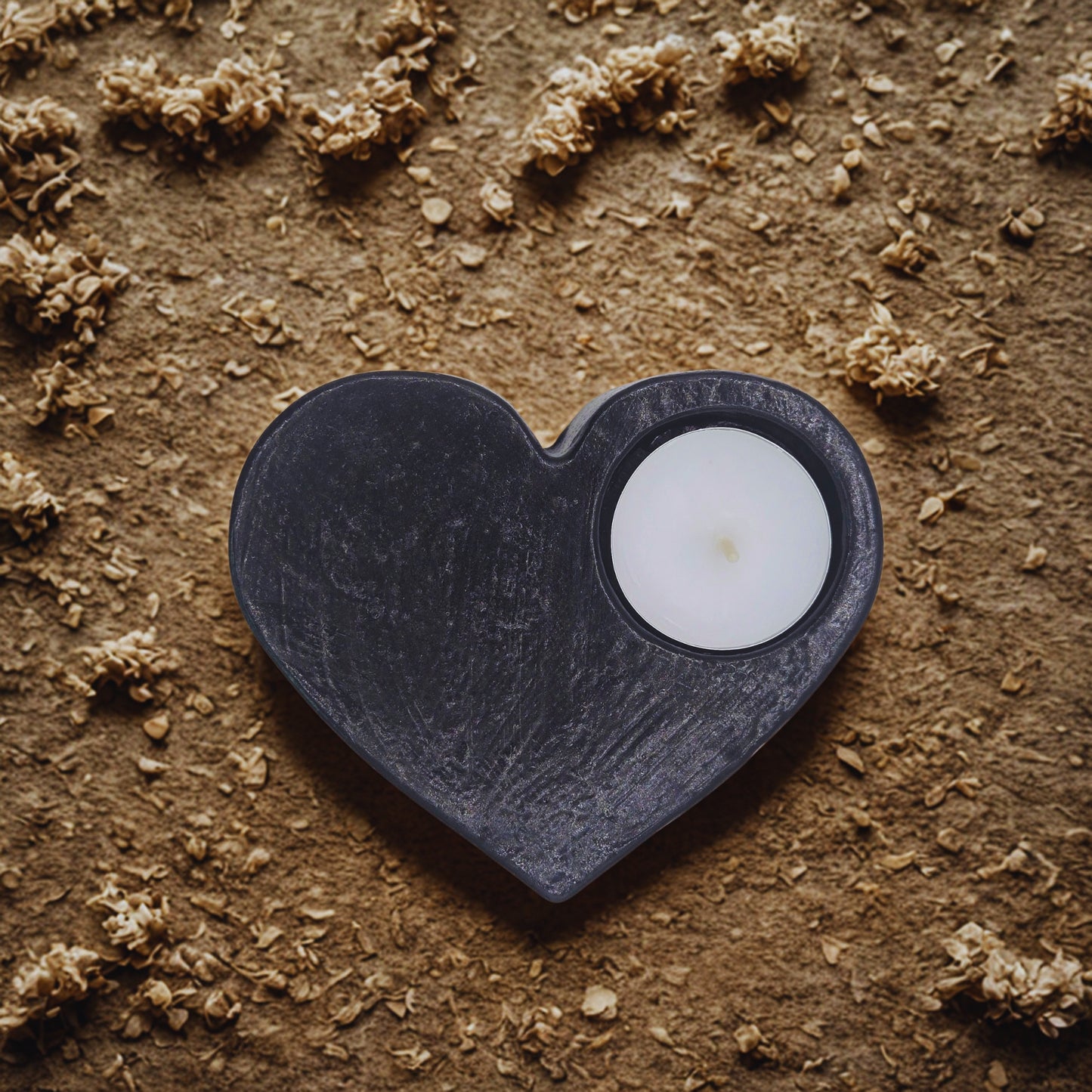 Heart-shaped black object with a white candle on a textured brown surface