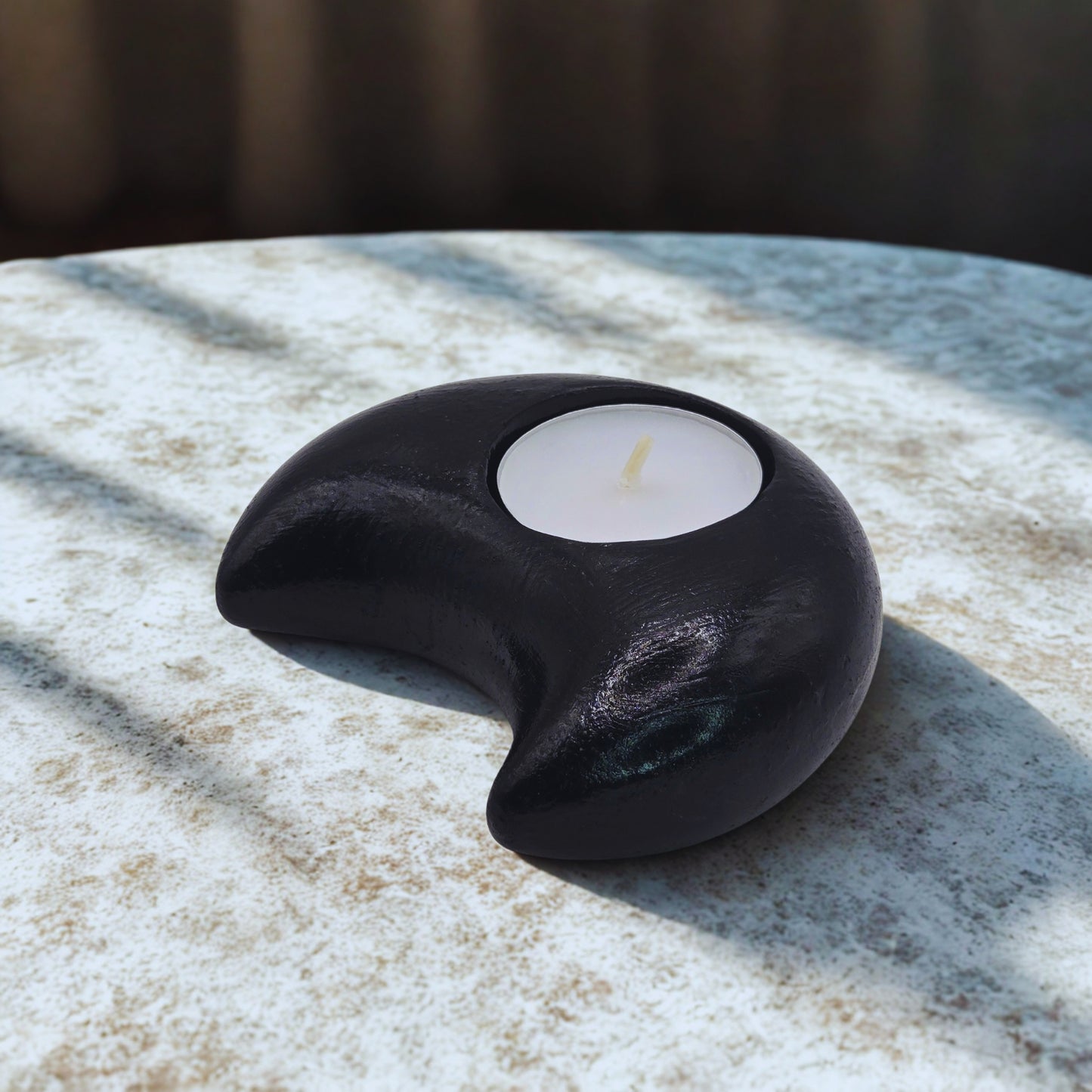 Black crescent-shaped candle holder with a white candle on a marble surface