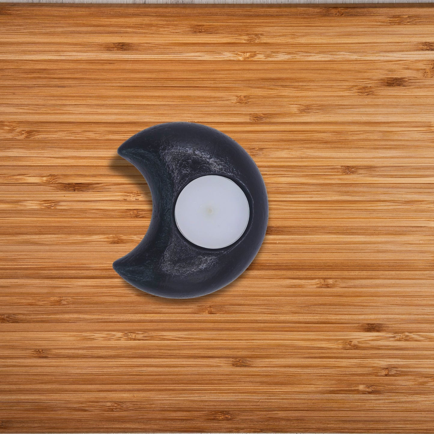 Black crescent moon-shaped candle holder with a white candle on a wooden surface