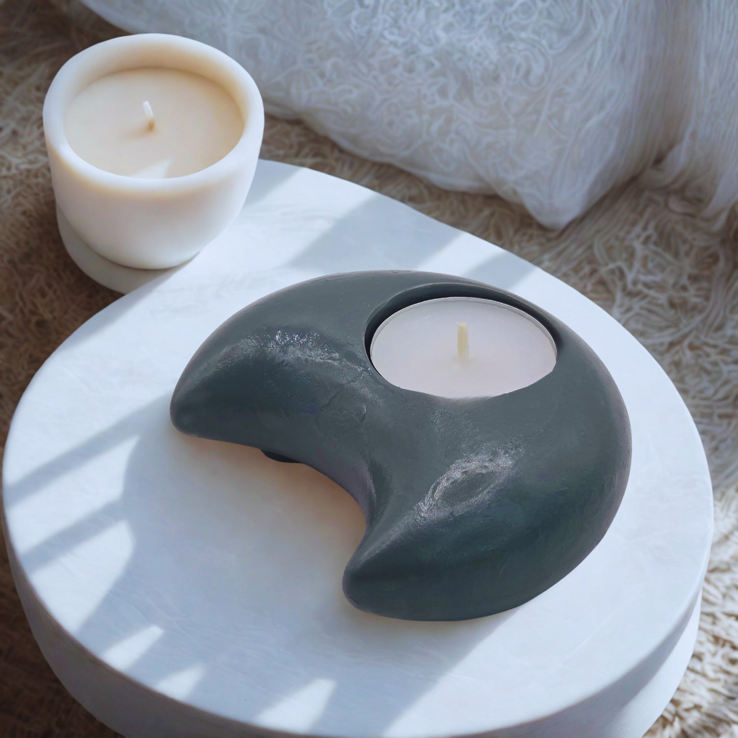 Moon tealight holder shaped like a yin and yang symbol with a candle inside, on a textured surface.