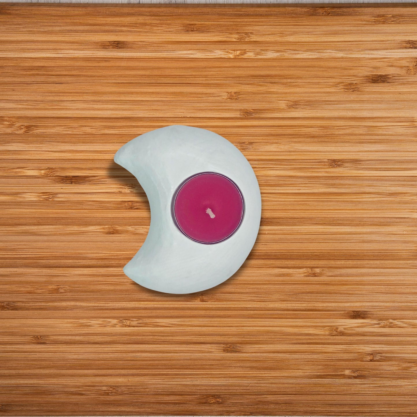 Pink candle in a white holder on a wooden surface