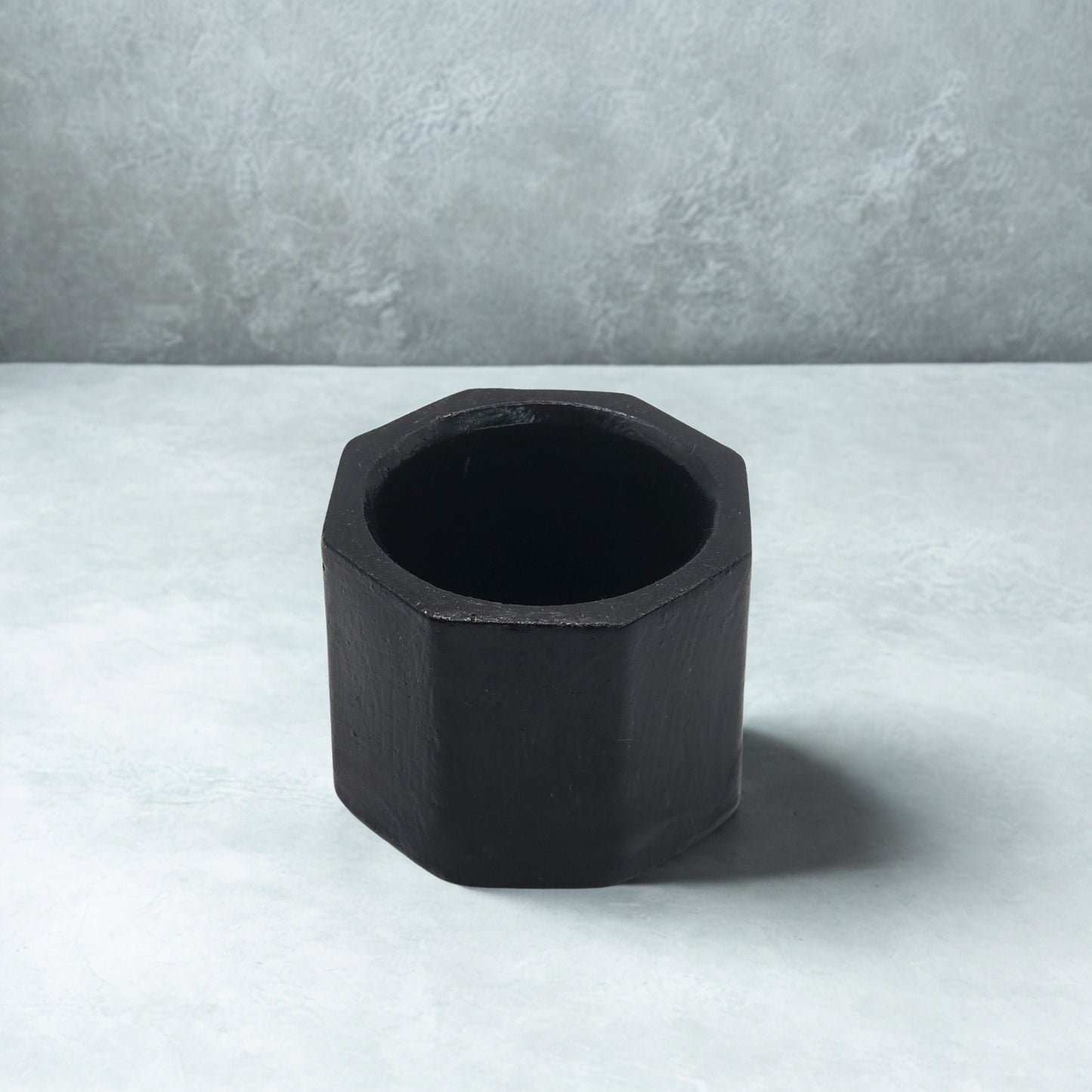 Black Octagon tealight holder on a light gray surface with a neutral gray background