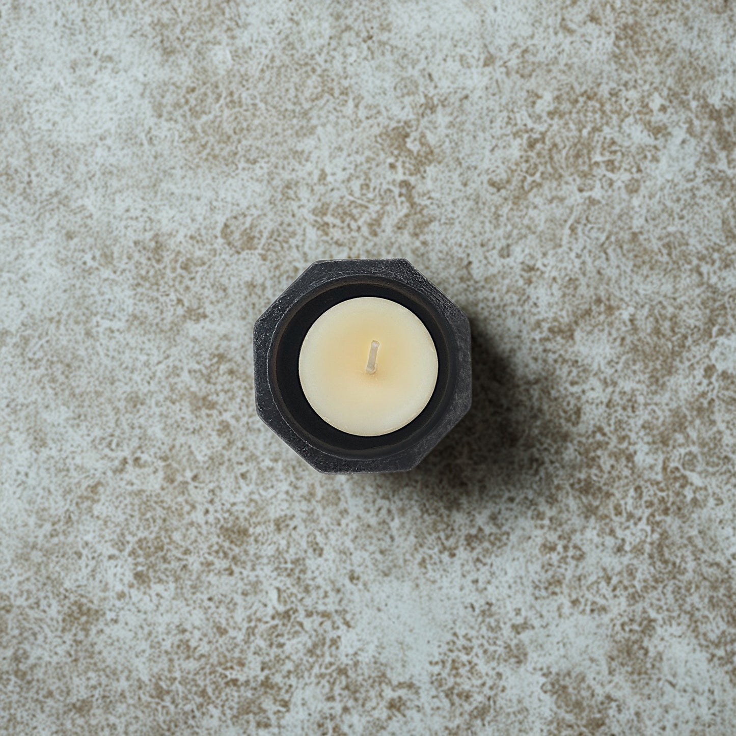 White candle in a black hexagonal holder on a textured stone surface