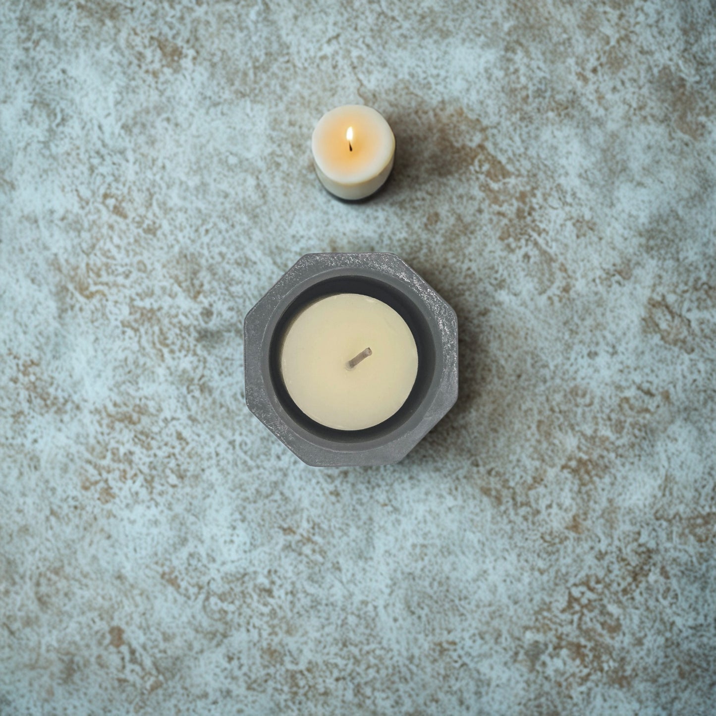 Two white candles in hexagonal holders on a textured stone surface