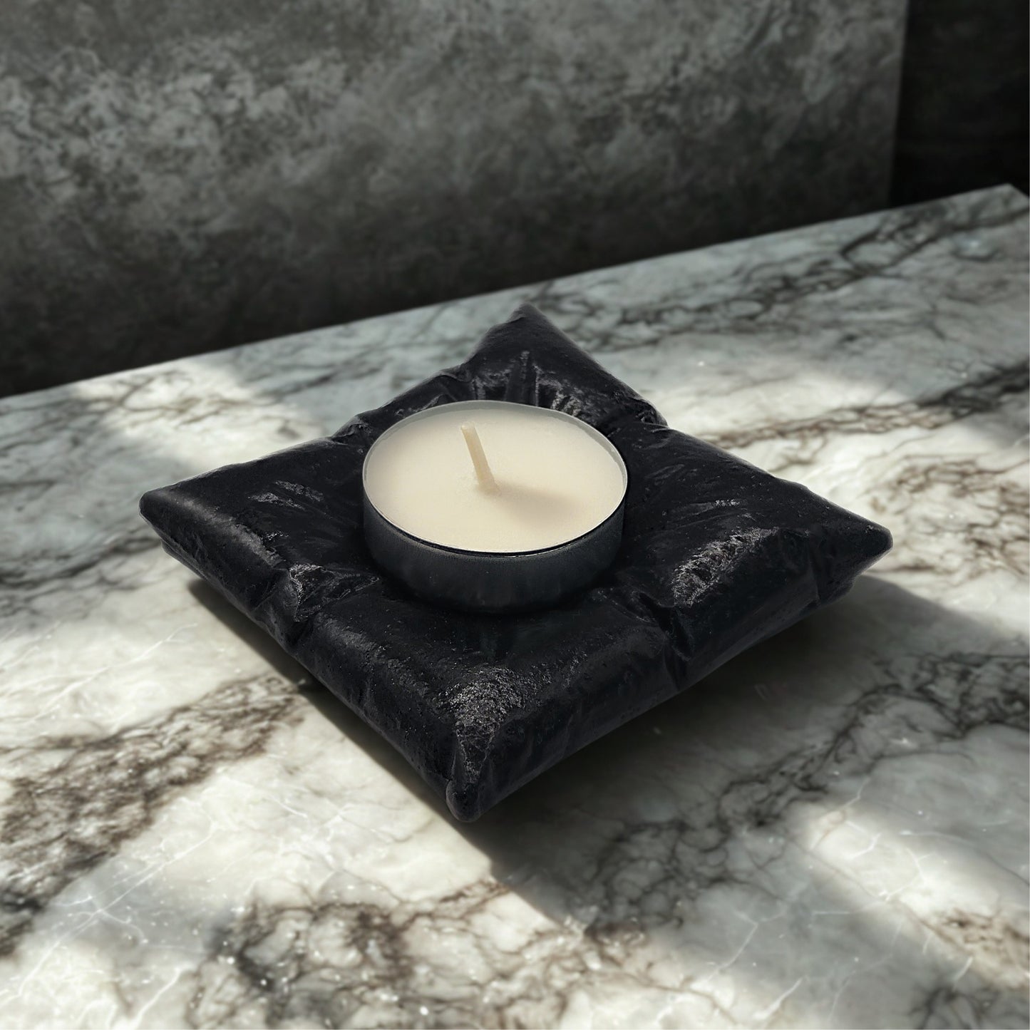 Black pillow tealight holder with a white candle on a marble surface
