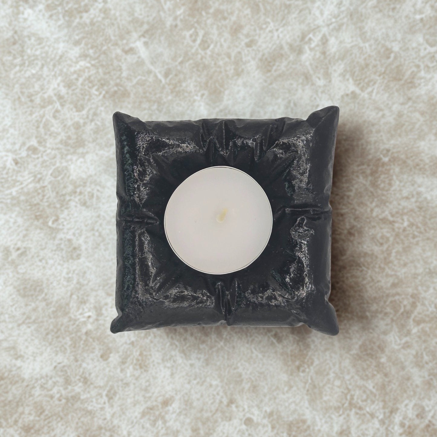 Black decorative candle holder with a white candle on a beige marble surface