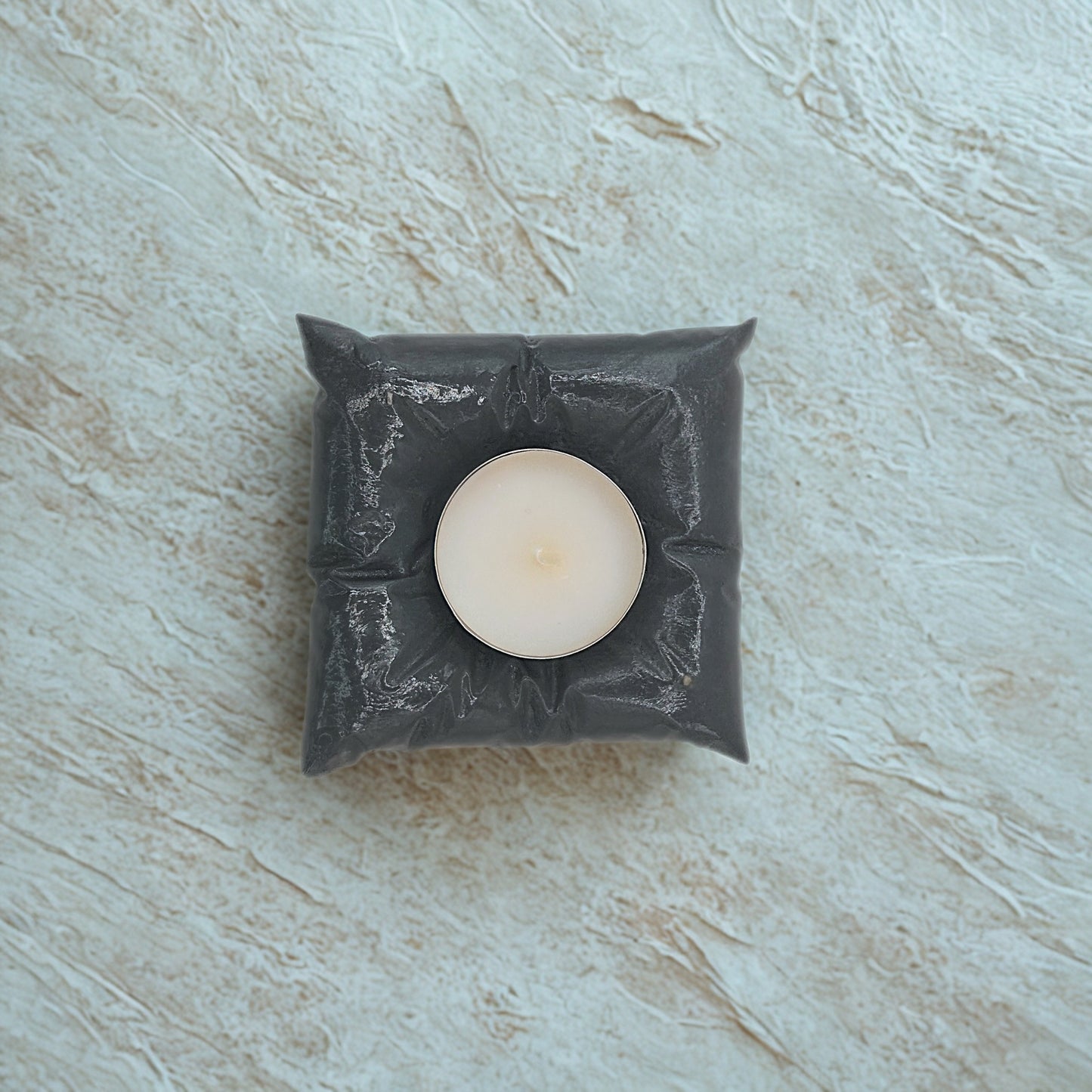 White candle in a decorative grey holder on a light marble surface