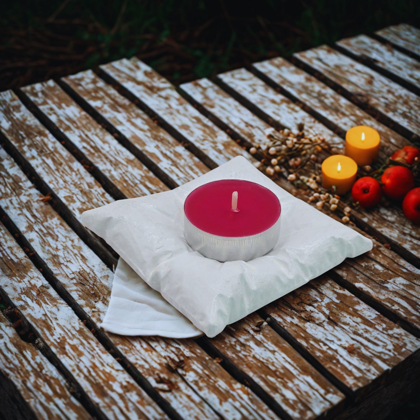 Pink candle on a white object with pine cones and apples on a wooden surface