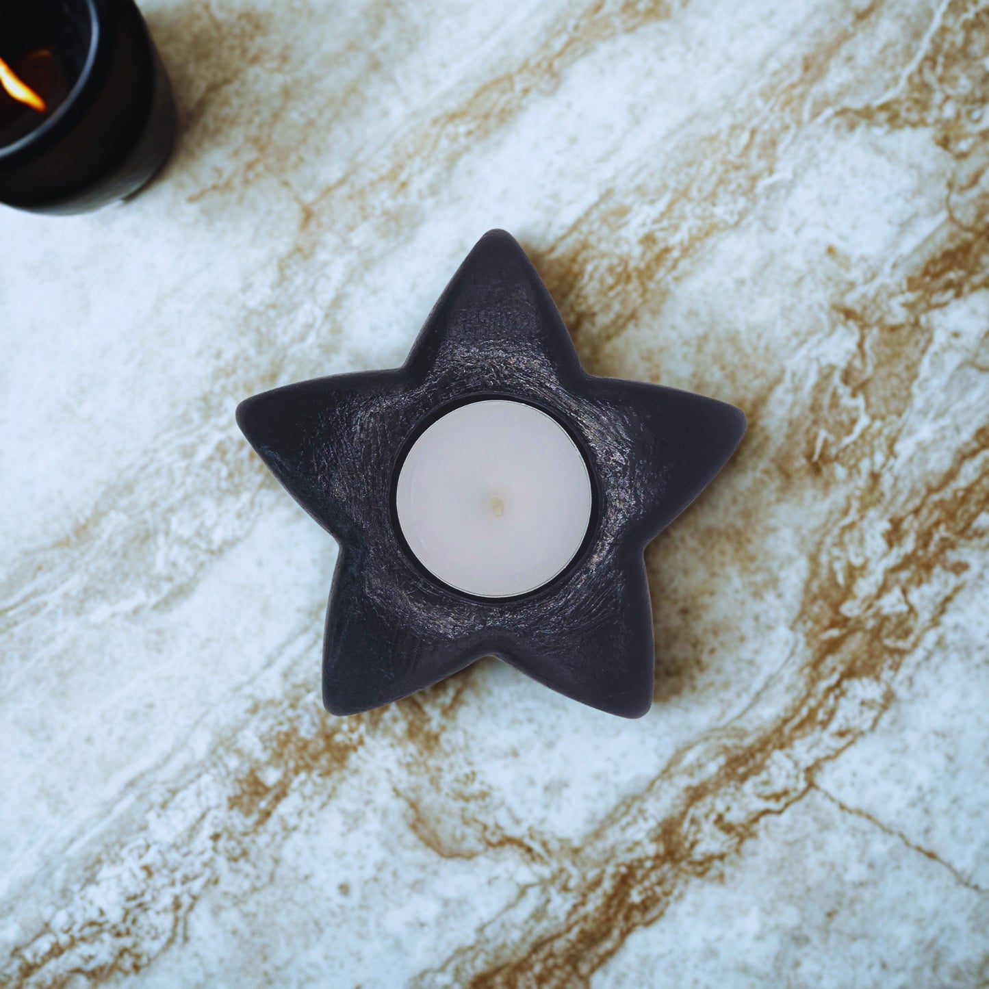 Star-shaped black candle holder with a lit candle on a marble surface