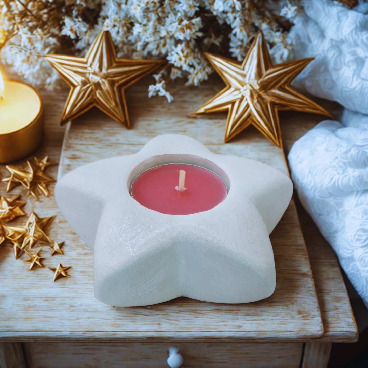 Star-shaped candle holder with a pink candle on a wooden surface, surrounded by decorative stars and flowers.
