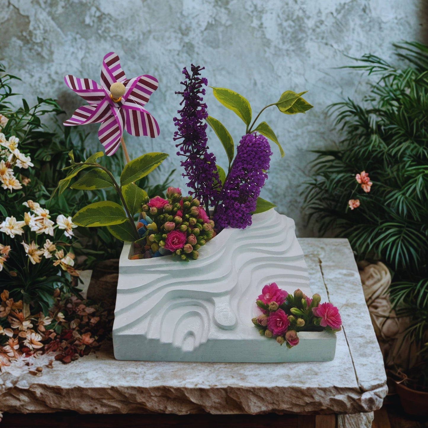 Decorative planter with flowers and a windmill on a stone surface with a garden background