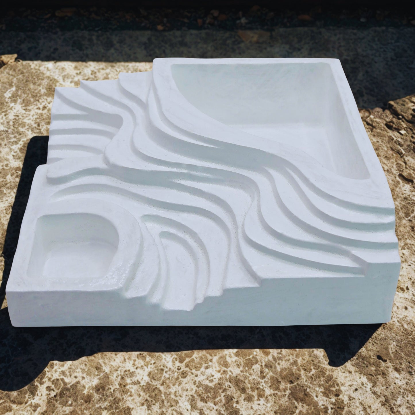 White object with wavy texture on a black stand against a natural stone background