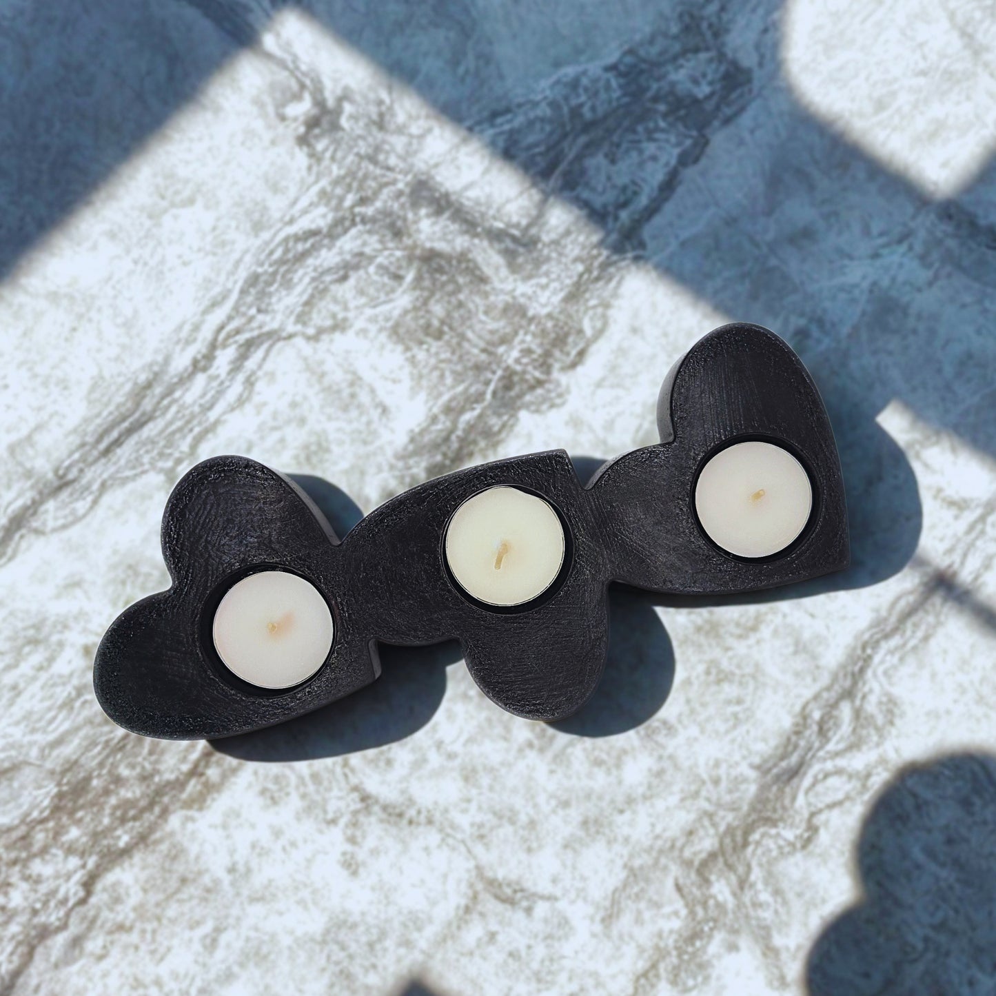 Three heart-shaped candle holders with candles on a marble surface