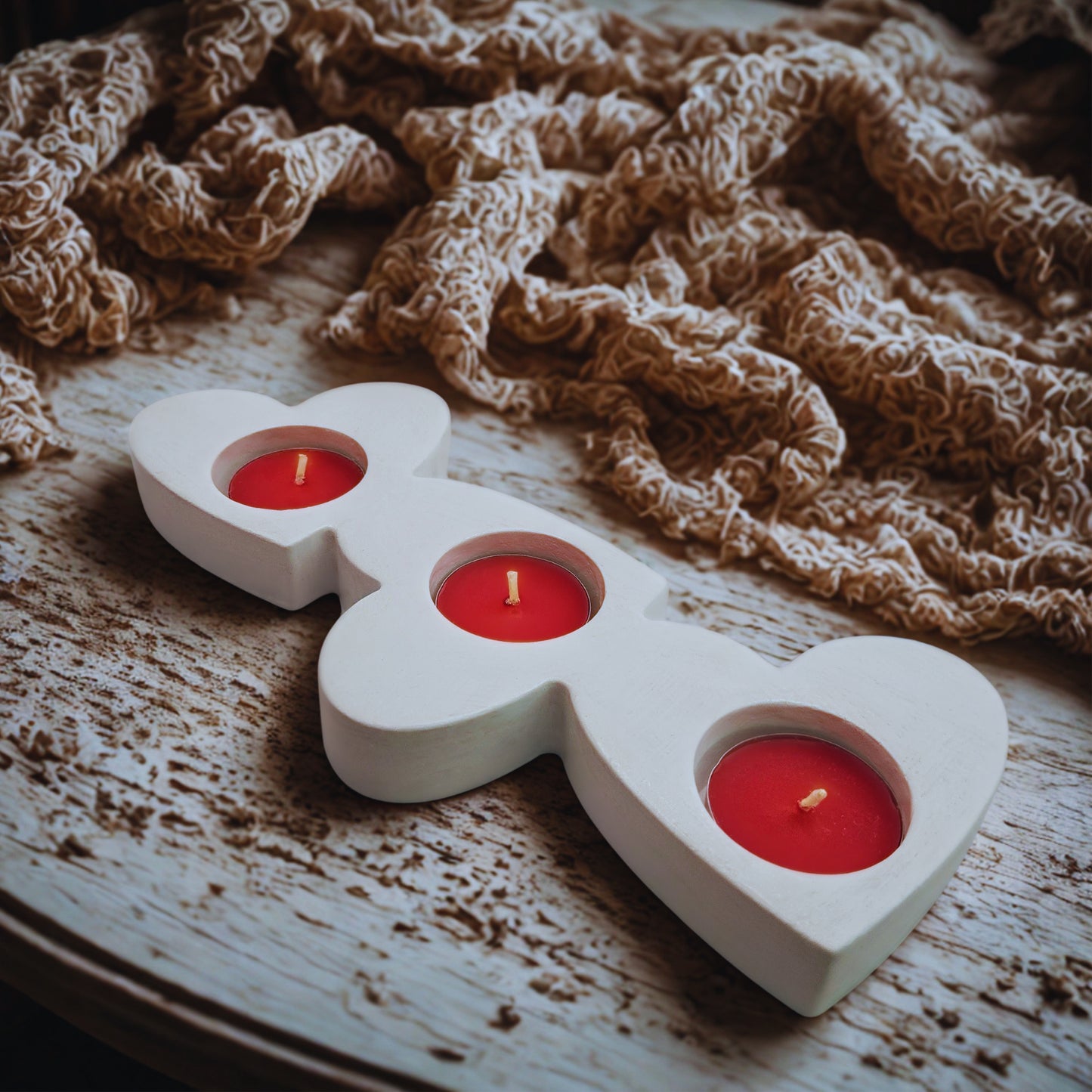 White candle holder shaped like a heart with three red candles on a wooden surface.