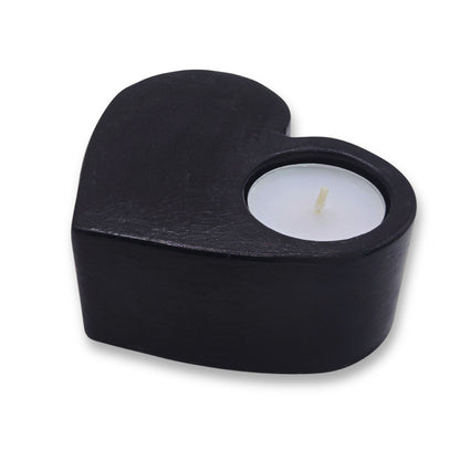 Black heart-shaped candle holder with a lit candle on a white background