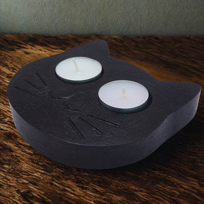 Black cat-shaped candle holder with two white candles on a wooden surface.