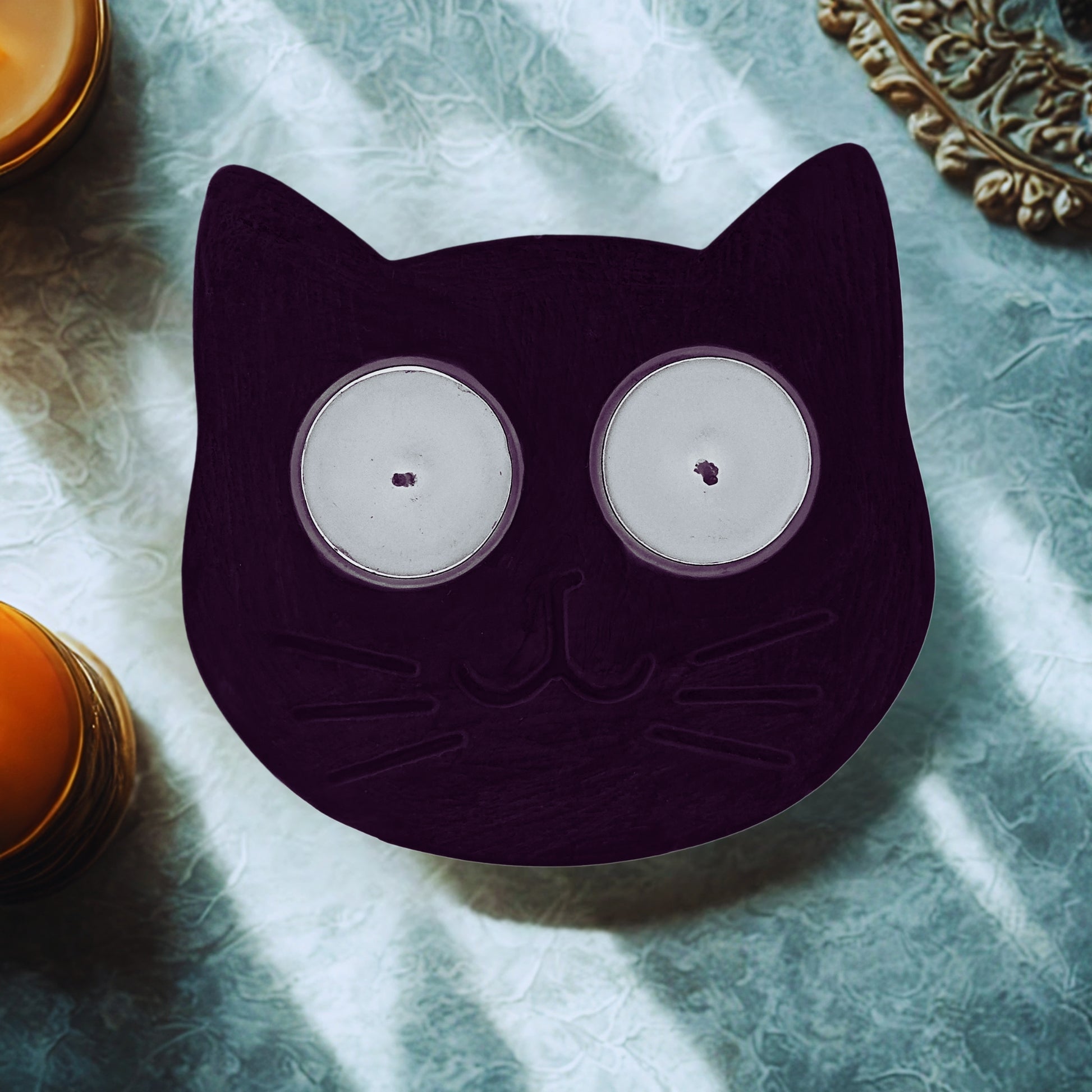 Cat-shaped candle holder with two candles on a textured surface