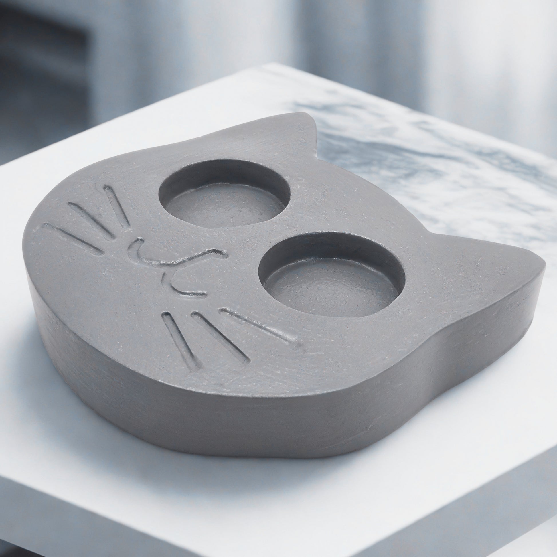 Gray shaped candle holder on a white surface with a blurred background