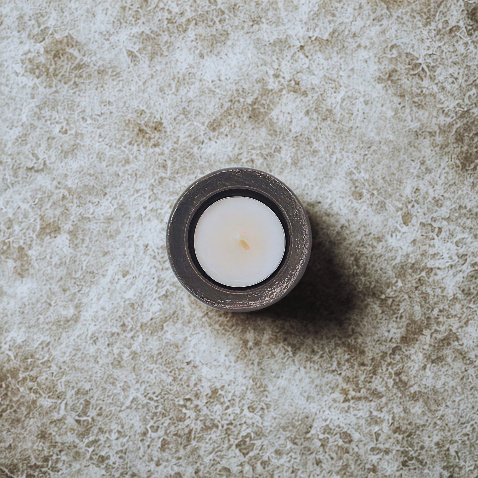 White candle in a dark holder on a textured stone surface