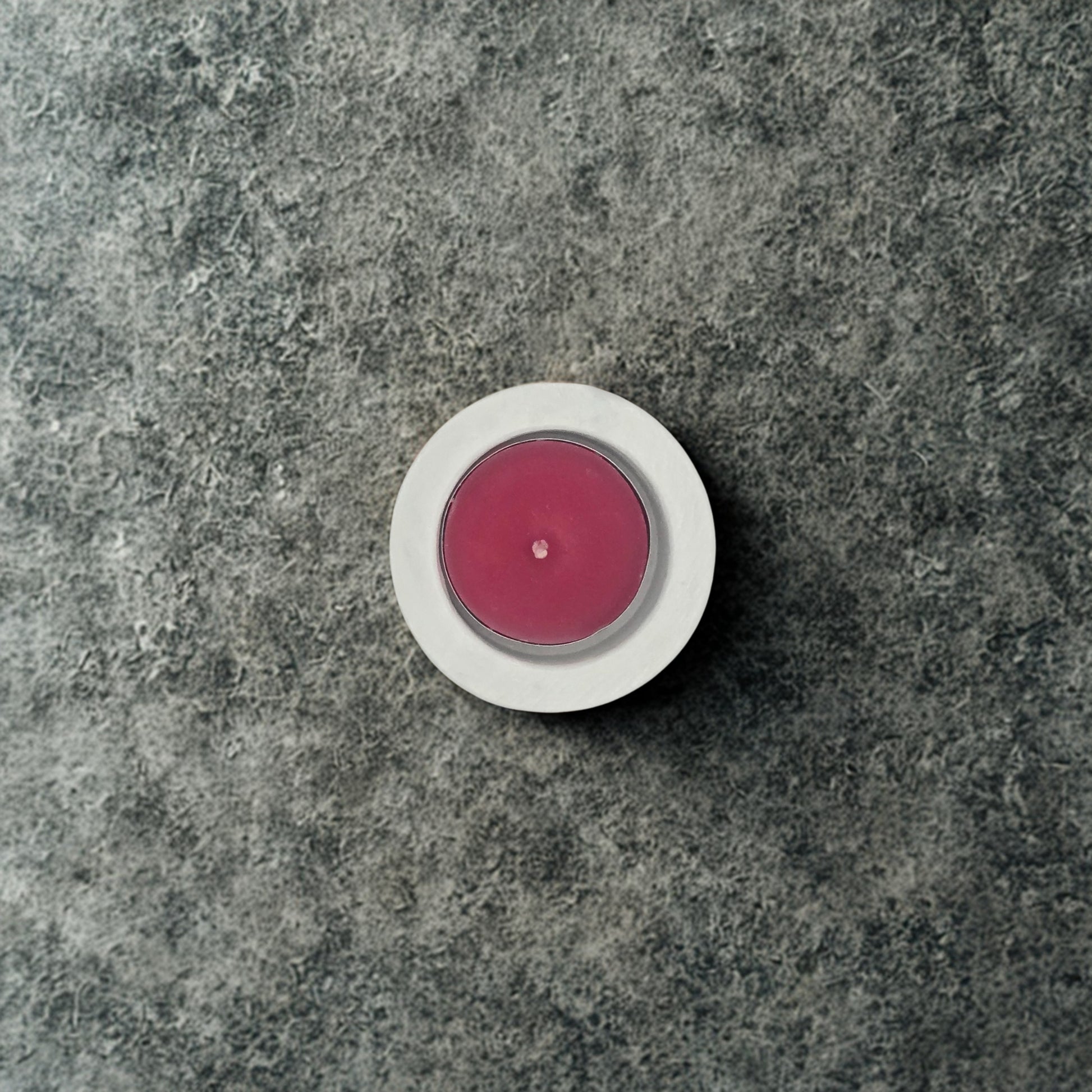 Pink candle in a white holder on a gray stone surface