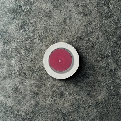 Pink candle in a white holder on a gray stone surface