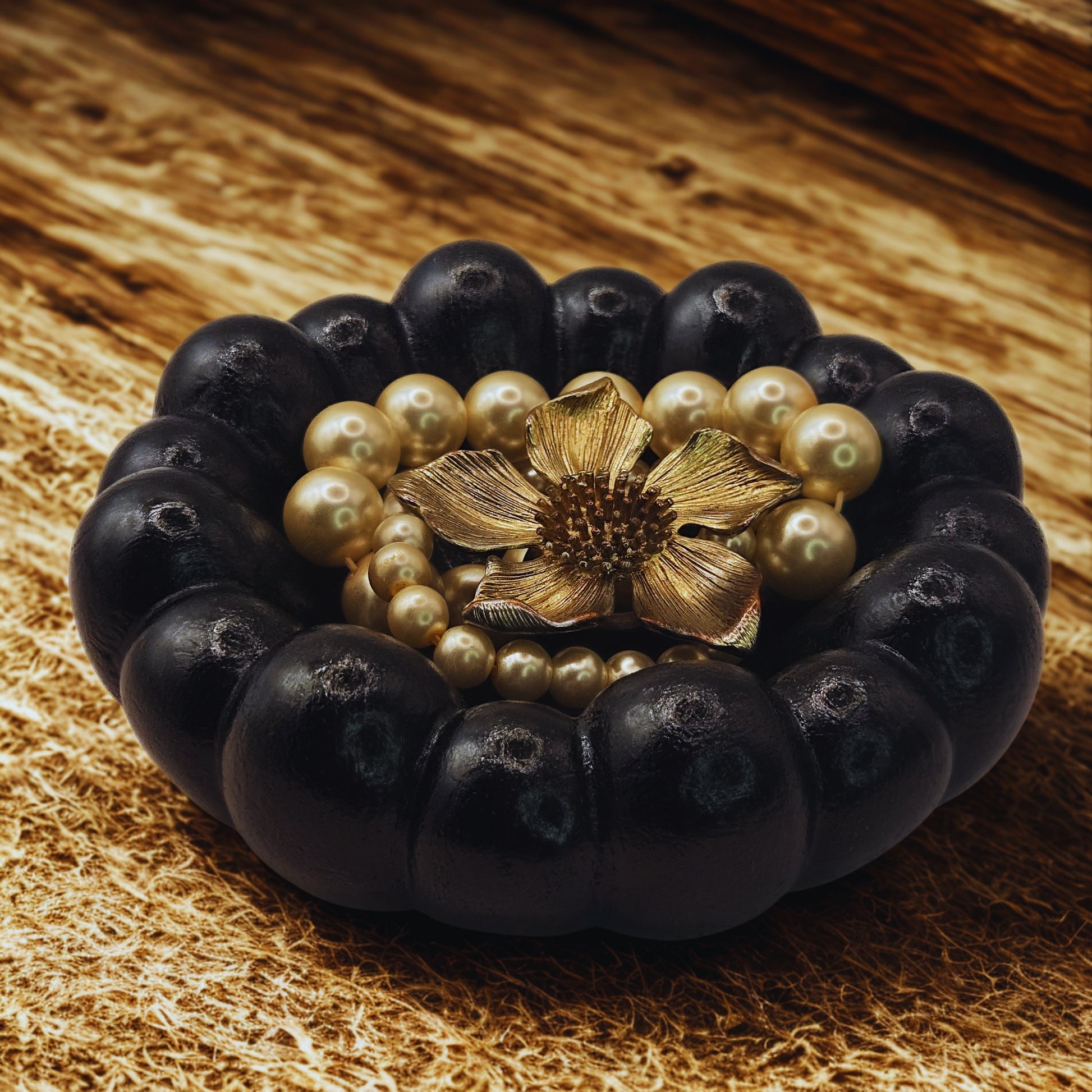 Black Cloud Jewellery Bowl with gold flower clasp and pearls on a wooden surface
