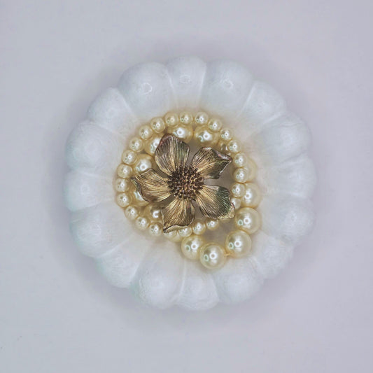 Decorative brooch with gold center and pearl accents on a white background