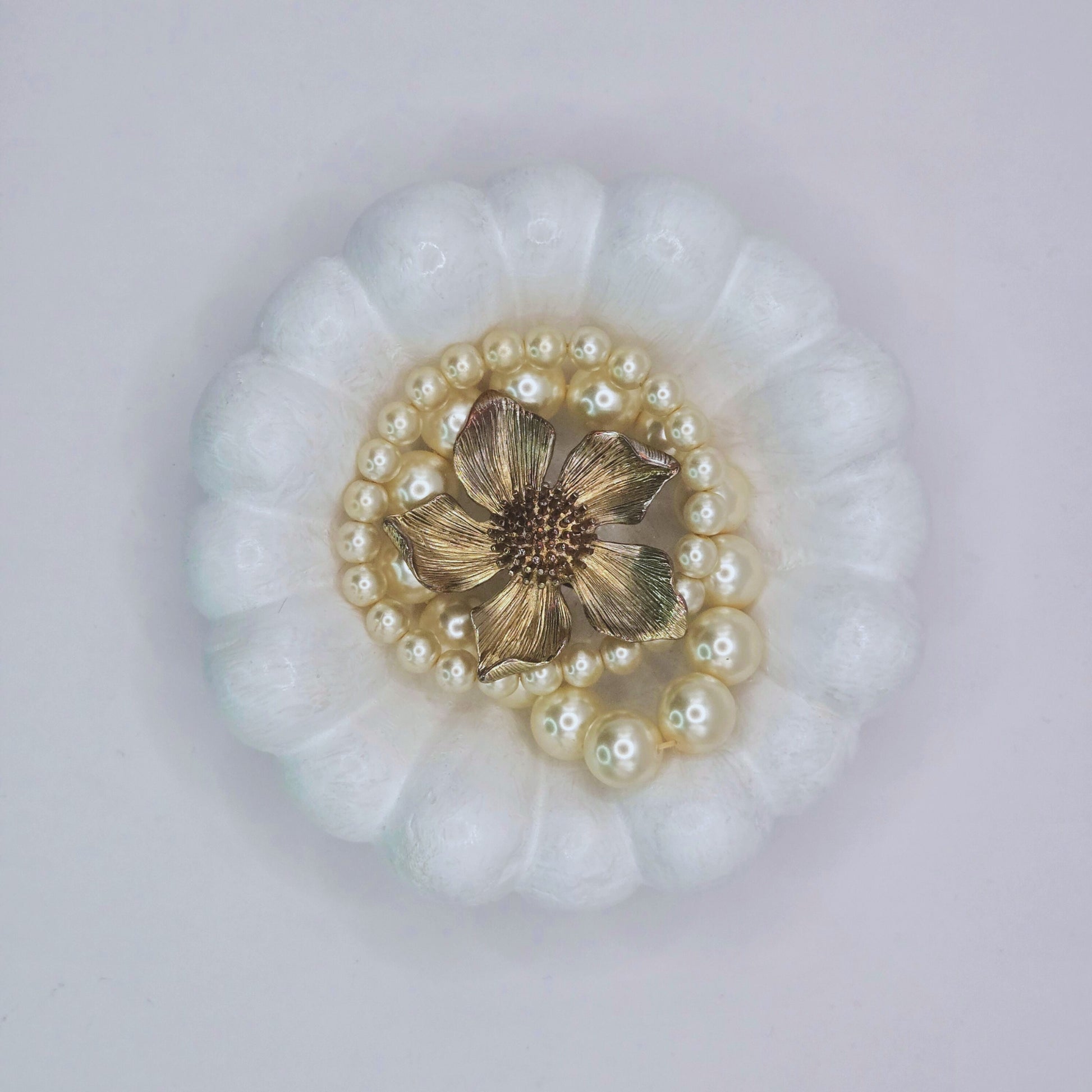 Decorative brooch with gold center and pearl accents on a white background