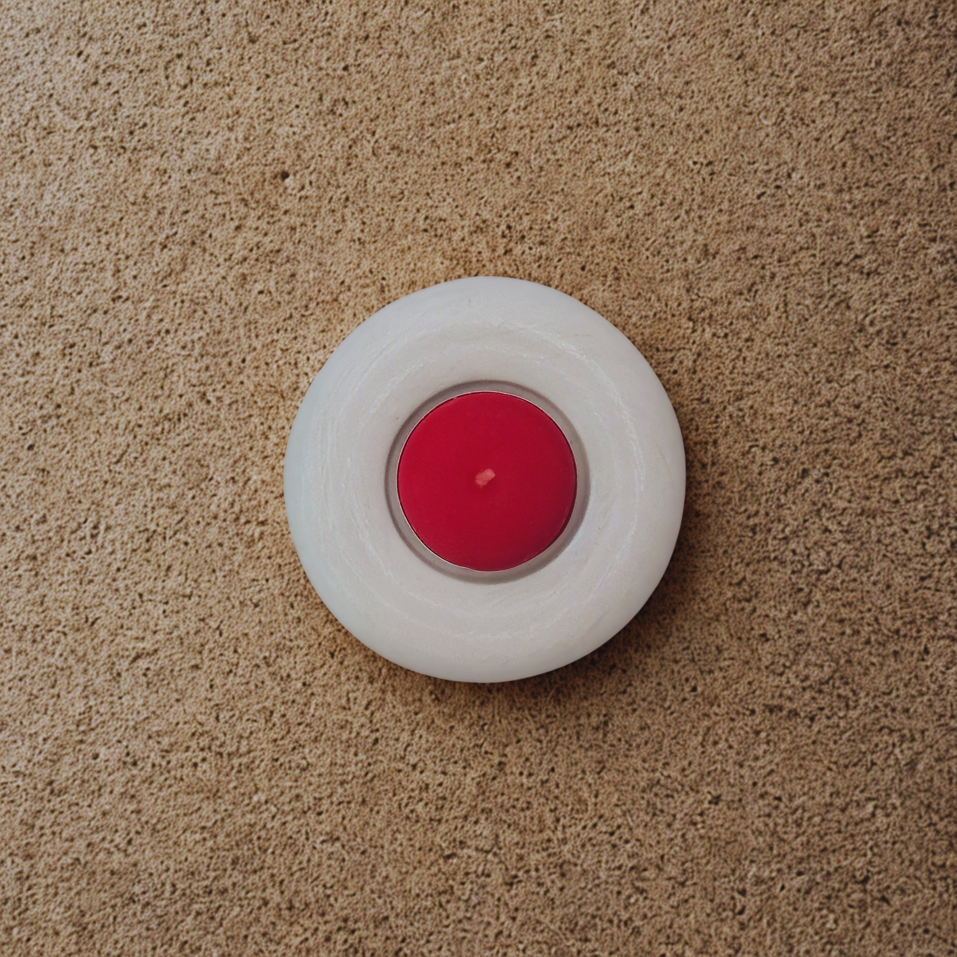 Red candle in a white holder on a beige carpet