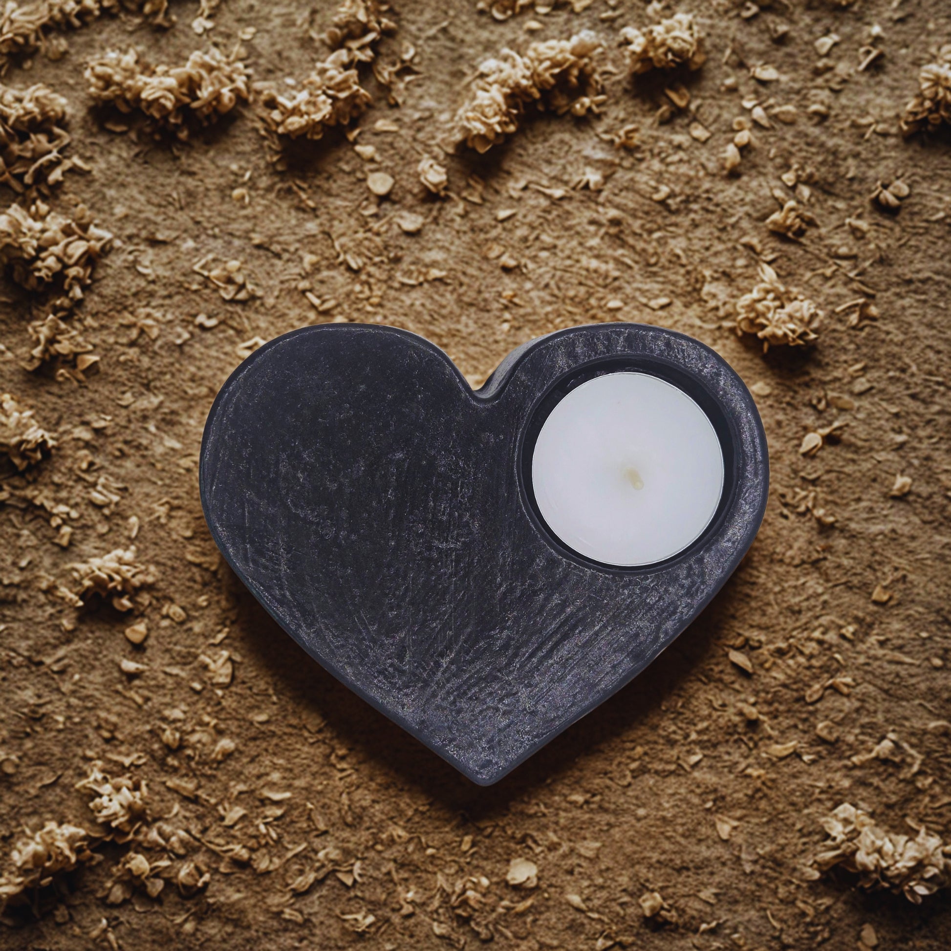 Heart-shaped black object with a white candle on a textured brown surface