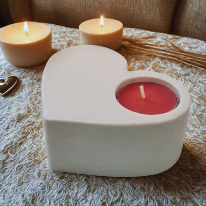 Heart-shaped candle holder with a red candle on a textured surface with two lit candles in the background.