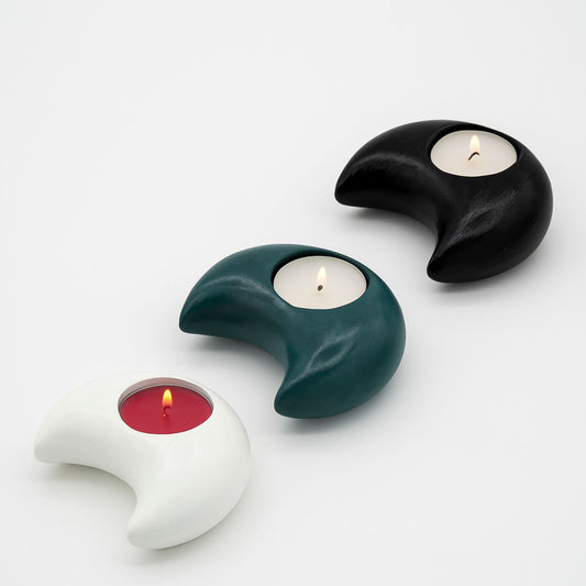 Three unique candle holders in black, green, and white with candles inside on a light gray background.