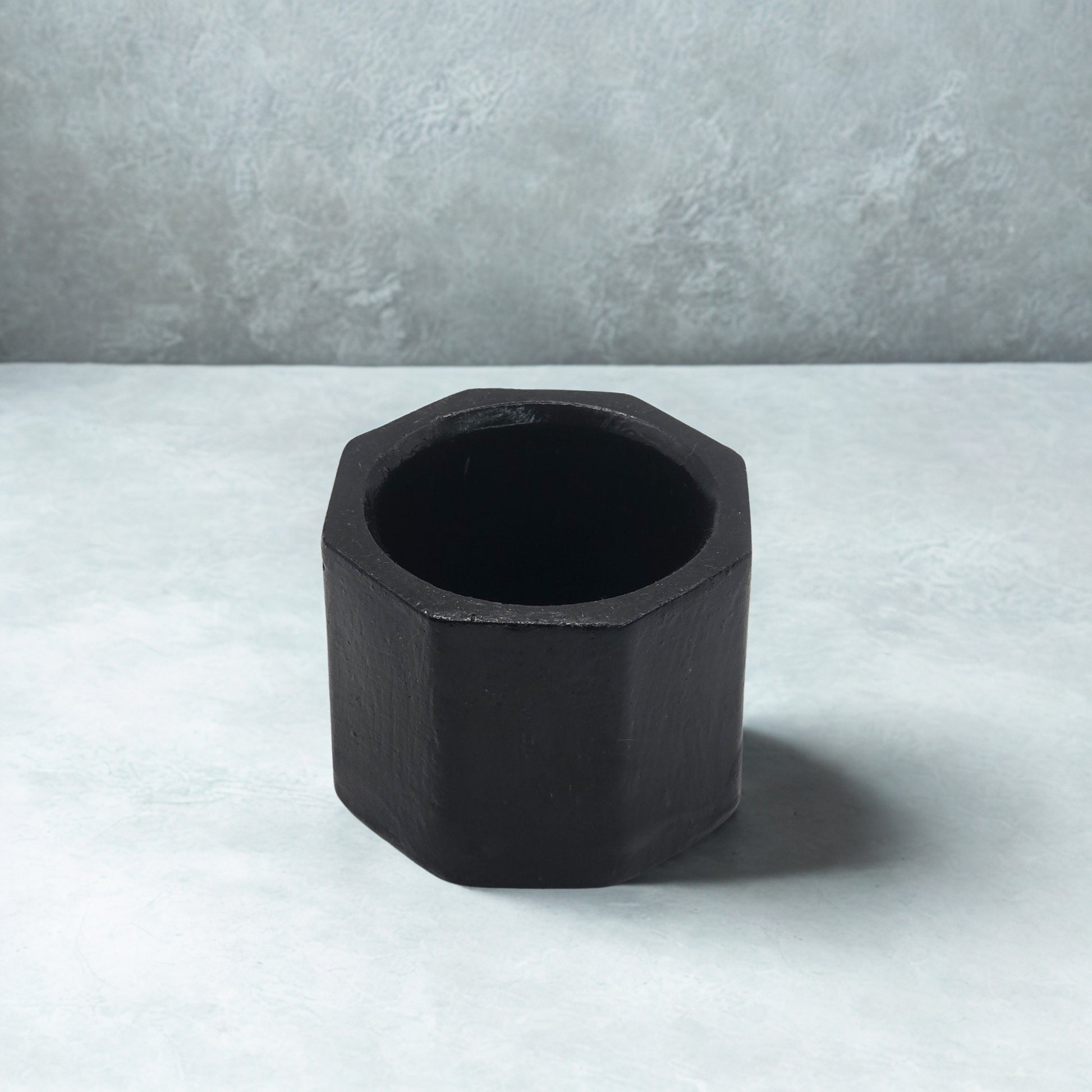 Black Octagon tealight holder on a light gray surface with a neutral gray background