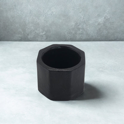 Black Octagon tealight holder on a light gray surface with a neutral gray background