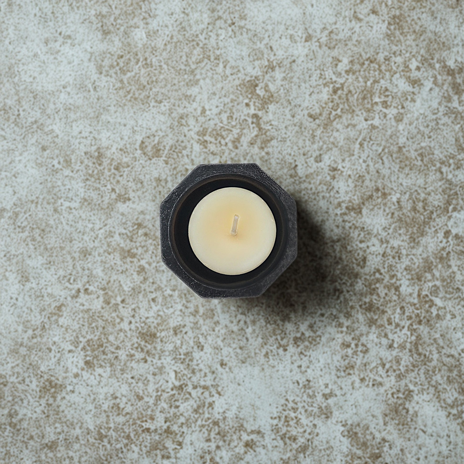 White candle in a black hexagonal holder on a textured stone surface
