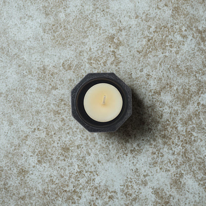 White candle in a black hexagonal holder on a textured stone surface