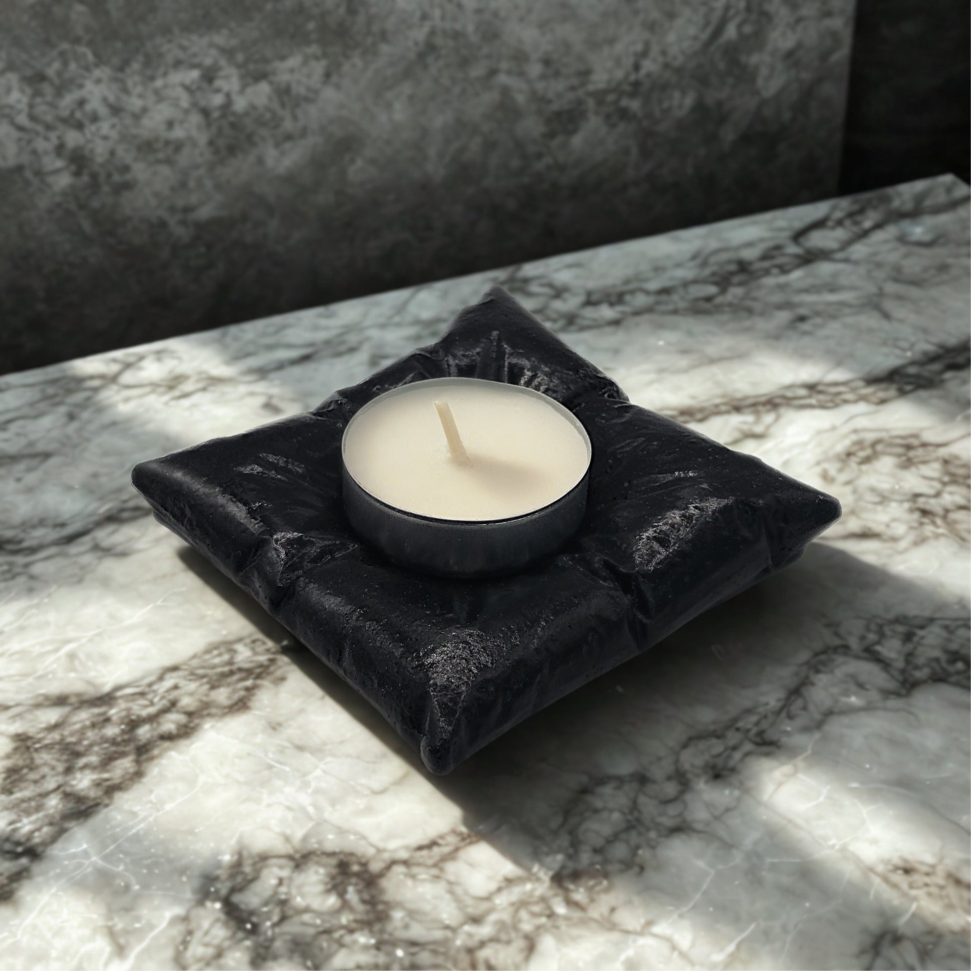 Black pillow tealight holder with a white candle on a marble surface